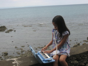 Maryan playing her “organ” on the sea wall behind her house